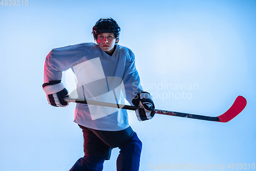 Image of Young male hockey player with the stick on ice court and white background in neon light