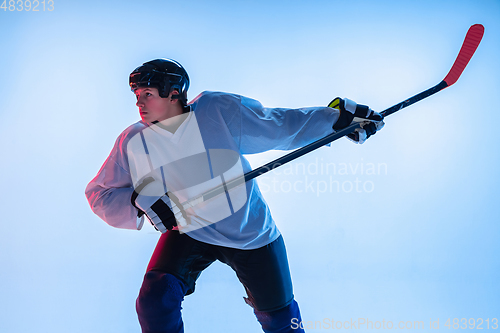 Image of Young male hockey player with the stick on ice court and white background in neon light