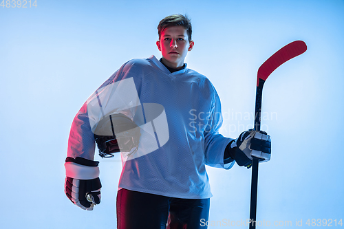 Image of Young male hockey player with the stick on ice court and white background in neon light