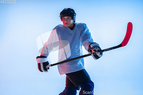 Image of Young male hockey player with the stick on ice court and white background in neon light