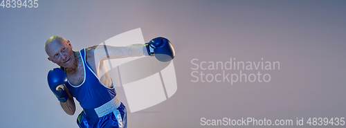 Image of Senior man wearing sportwear boxing isolated on gradient studio background in neon light. Concept of sport, activity, movement, wellbeing. Copyspace, ad.