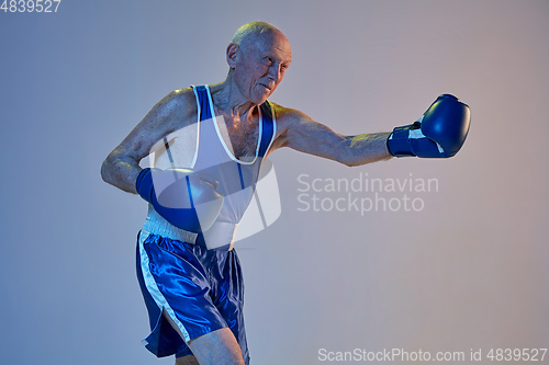 Image of Senior man wearing sportwear boxing isolated on gradient studio background in neon light. Concept of sport, activity, movement, wellbeing. Copyspace, ad.