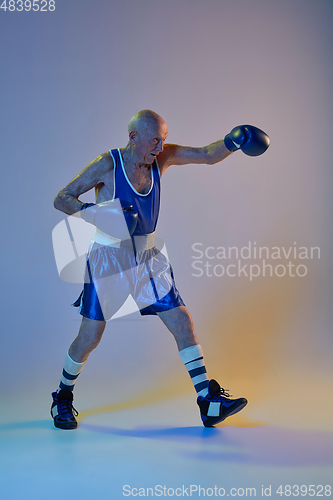 Image of Senior man wearing sportwear boxing isolated on gradient studio background in neon light. Concept of sport, activity, movement, wellbeing. Copyspace, ad.