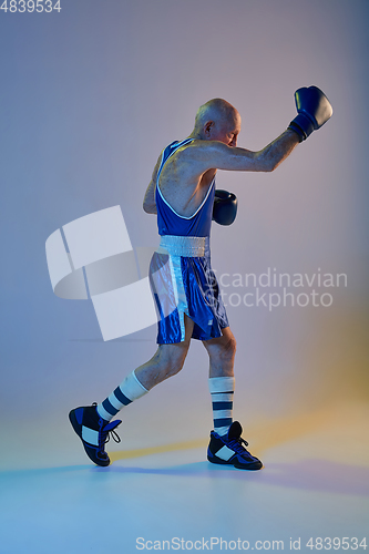 Image of Senior man wearing sportwear boxing isolated on gradient studio background in neon light. Concept of sport, activity, movement, wellbeing. Copyspace, ad.