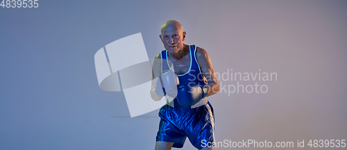 Image of Senior man wearing sportwear boxing isolated on gradient studio background in neon light. Concept of sport, activity, movement, wellbeing. Copyspace, ad.