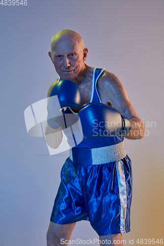 Image of Senior man wearing sportwear boxing isolated on gradient studio background in neon light. Concept of sport, activity, movement, wellbeing. Copyspace, ad.