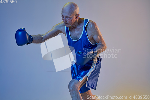 Image of Senior man wearing sportwear boxing isolated on gradient studio background in neon light. Concept of sport, activity, movement, wellbeing. Copyspace, ad.