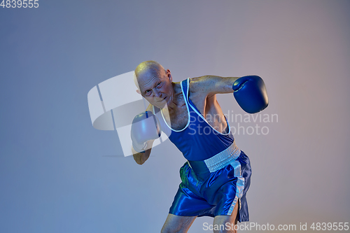 Image of Senior man wearing sportwear boxing isolated on gradient studio background in neon light. Concept of sport, activity, movement, wellbeing. Copyspace, ad.