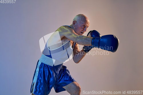 Image of Senior man wearing sportwear boxing isolated on gradient studio background in neon light. Concept of sport, activity, movement, wellbeing. Copyspace, ad.