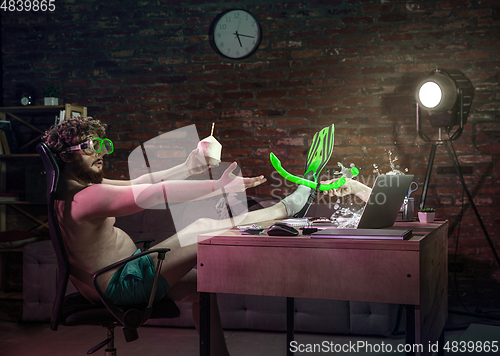 Image of Young man drinking cocktail during online meeting with friends.