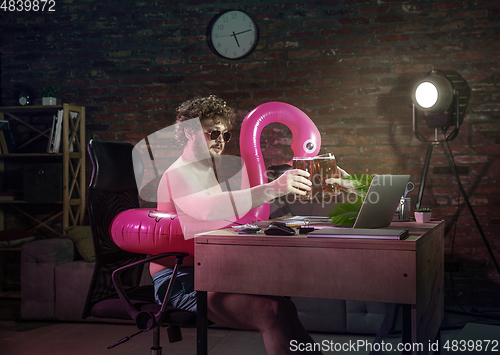 Image of Young man drinking beer during online meeting with friends on video call.