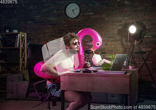 Image of Young man drinking cocktail during online meeting with friends.