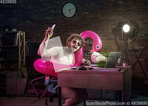 Image of Young man drinking cocktail during online meeting with friends.