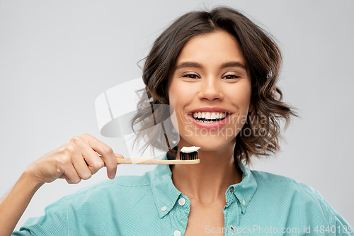 Image of smiling woman with toothpaste on wooden toothbrush