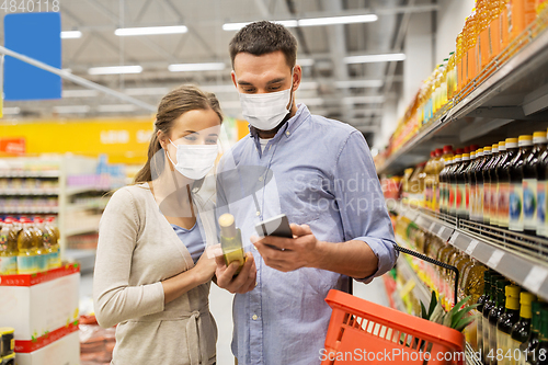 Image of couple in masks with phone and olive oil at store