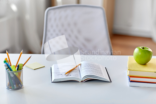 Image of books, apple and school supplies on table at home