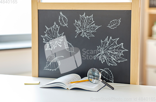 Image of book with magnifier on table and chalkboard