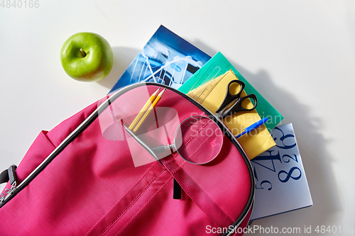 Image of backpack with books, school supplies and apple