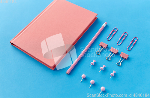 Image of pink notebook, pins, clips and pencil on blue