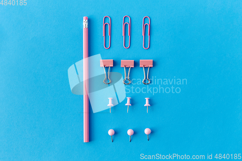 Image of pink pencil, pins and clips on blue background