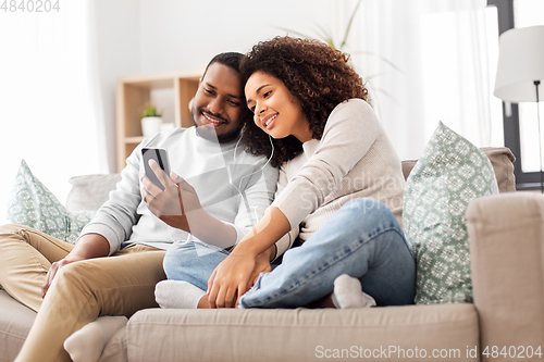 Image of happy couple with smartphone and earphones at home
