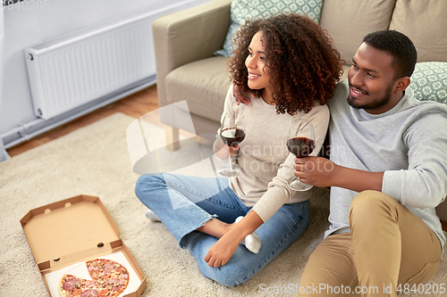 Image of happy couple with wine and takeaway pizza at home