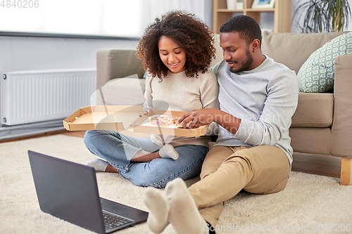 Image of happy african american couple eating pizza at home