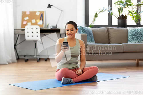 Image of woman with smartphone sits on exercise mat at home