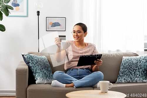 Image of happy woman with tablet pc and credit card at home