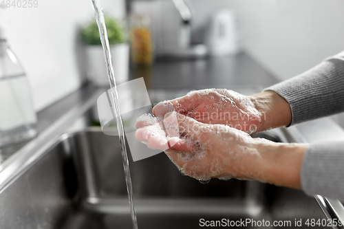 Image of woman washing hands with liquid soap in kitchen