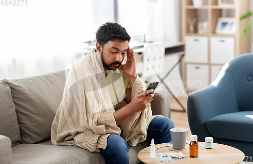 Image of sick young man in blanket with smartphone at home