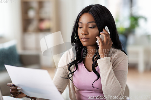 Image of woman with papers calling on phone at home office