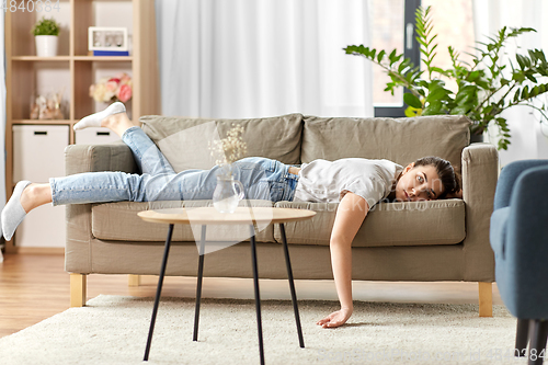 Image of bored or lazy young woman lying on sofa at home