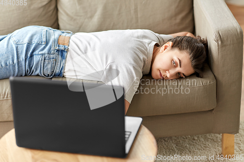 Image of bored woman with laptop lying on sofa at home