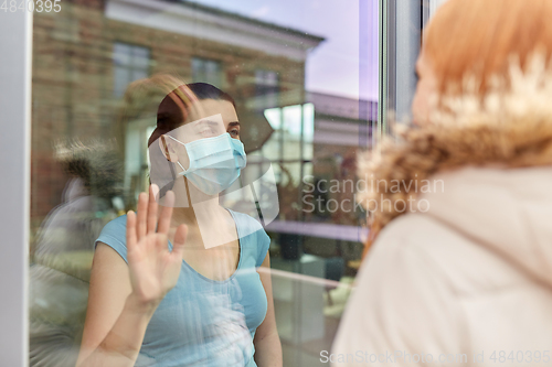 Image of ill woman in mask looking at friend through window