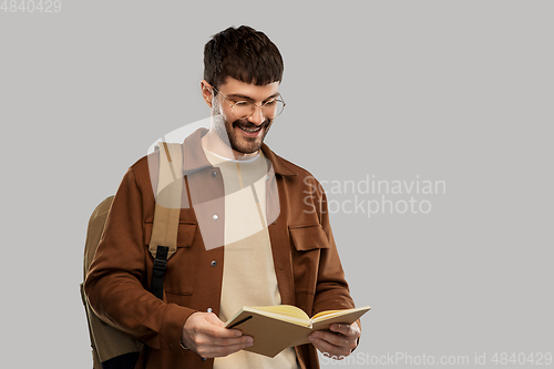 Image of smiling young man with backpack reading diary