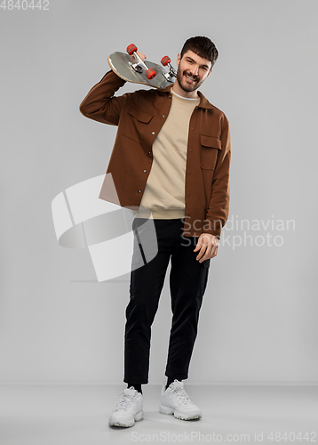 Image of smiling young man in brown jacket with skateboard