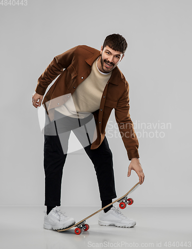 Image of smiling young man in brown jacket with skateboard