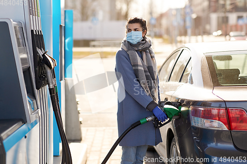 Image of woman in mask filling her car at gas station