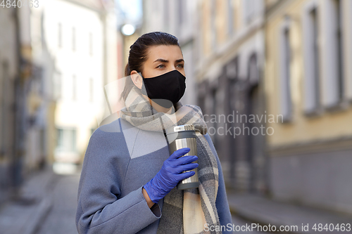 Image of woman in reusable mask with tumbler in city