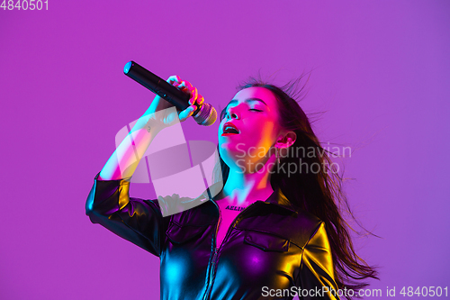 Image of Caucasian female singer portrait isolated on purple studio background in neon light