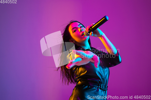 Image of Caucasian female singer portrait isolated on purple studio background in neon light