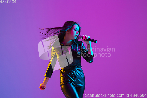 Image of Caucasian female singer portrait isolated on purple studio background in neon light