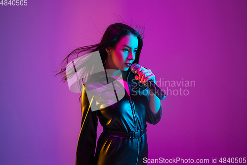 Image of Caucasian female singer portrait isolated on purple studio background in neon light