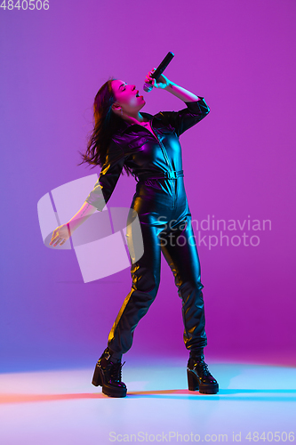 Image of Caucasian female singer portrait isolated on purple studio background in neon light