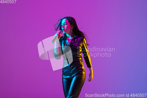 Image of Caucasian female singer portrait isolated on purple studio background in neon light