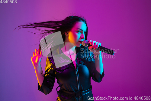 Image of Caucasian female singer portrait isolated on purple studio background in neon light