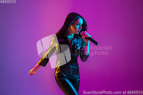 Image of Caucasian female singer portrait isolated on purple studio background in neon light