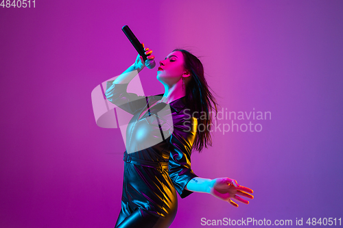 Image of Caucasian female singer portrait isolated on purple studio background in neon light