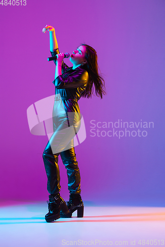 Image of Caucasian female singer portrait isolated on purple studio background in neon light